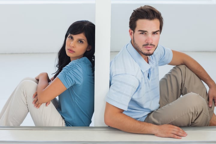 Unhappy couple are separated by white wall and looking camera