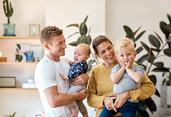 Glückliches Paar mit ihren 2 Kindern am Arm im Wohnzimmer